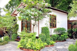 A small white building with a sloped roof, surrounded by lush greenery and a gravel path. - Anna River Home A3 (Bangkok)