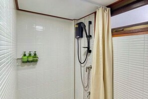 A bathroom with white tiled walls, a shower with a beige curtain, and a shelf with green bottles. - Anna River Home A3 (Bangkok)