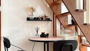 A modern interior with a round table, two chairs, a wooden staircase, and a shelf with decorative items. - Anna River Home A3 (Bangkok)