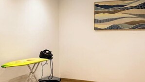 A room with a single bed, a wall-mounted artwork, and a small ironing board with an iron.