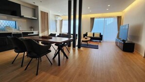 Ein modernes Wohnzimmer mit einem Holzesstisch, schwarzen Stühlen, einer Couch und einem Fernseher.