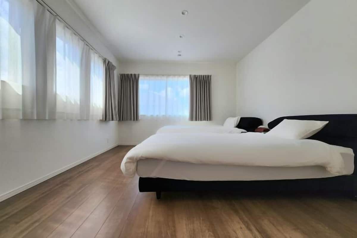 Un dormitorio con cama, ventana con cortinas y suelo de madera.