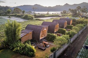 A row of wooden cabins with a patio area, surrounded by greenery and a view of the landscape. - Tegal Bamboo Cottages & Private Hot Spring (Bali)