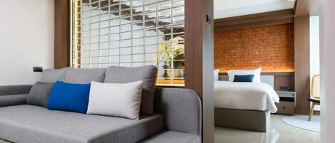 A modern hotel room with a grey sofa, a bed with white bedding, and a brick wall.