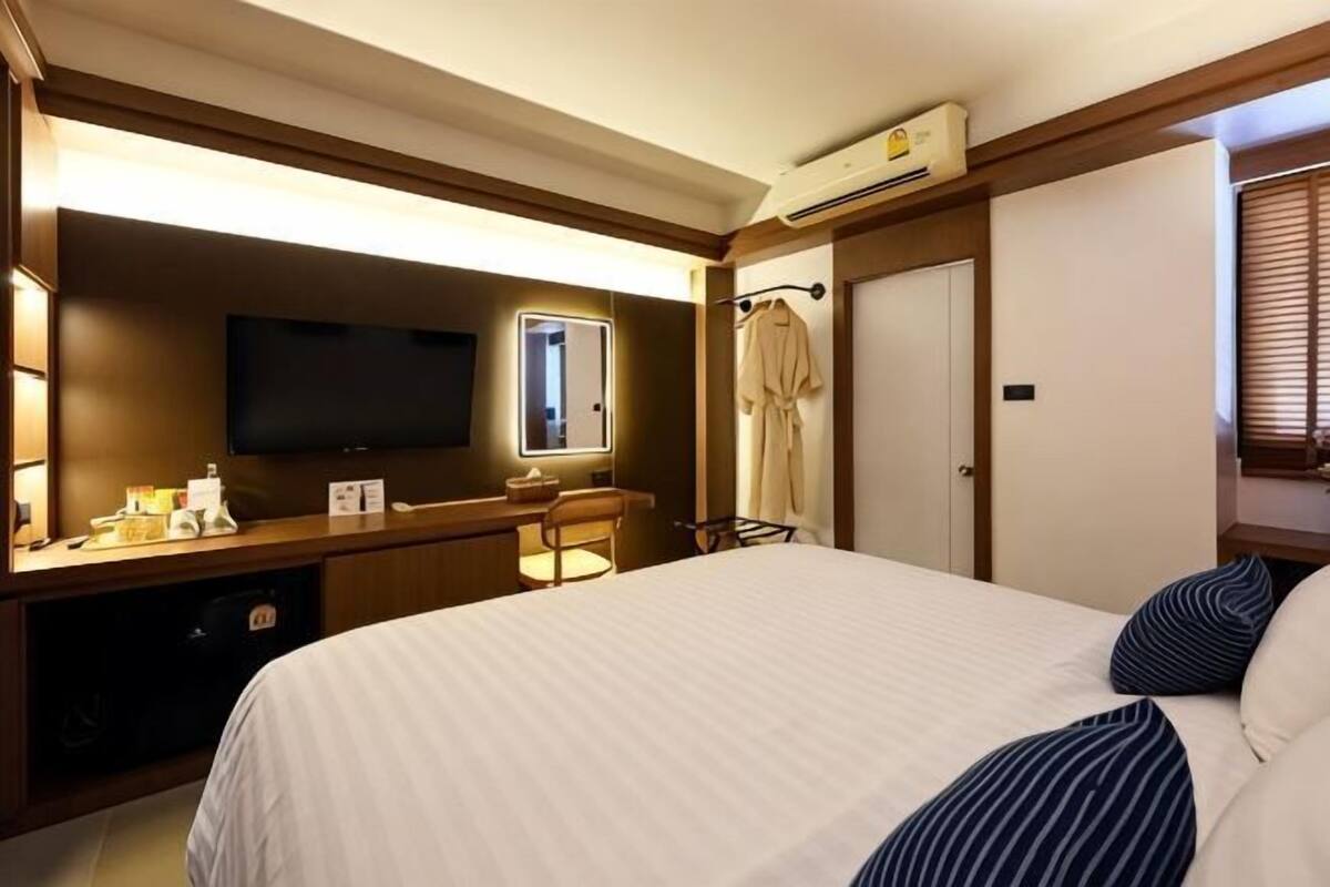 Une chambre d’hôtel comprenant un lit, un bureau avec un téléviseur à écran plat, un miroir, un peignoir et une porte.