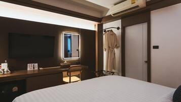 A hotel room with a bed, a desk, a chair, a television, a mirror, a wardrobe, and an air conditioning unit.