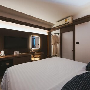 A hotel room with a bed, a desk, a chair, a television, a mirror, a wardrobe, and an air conditioning unit. - Wangkaew Hotel, Phitsanulok (Phitsanulok)
