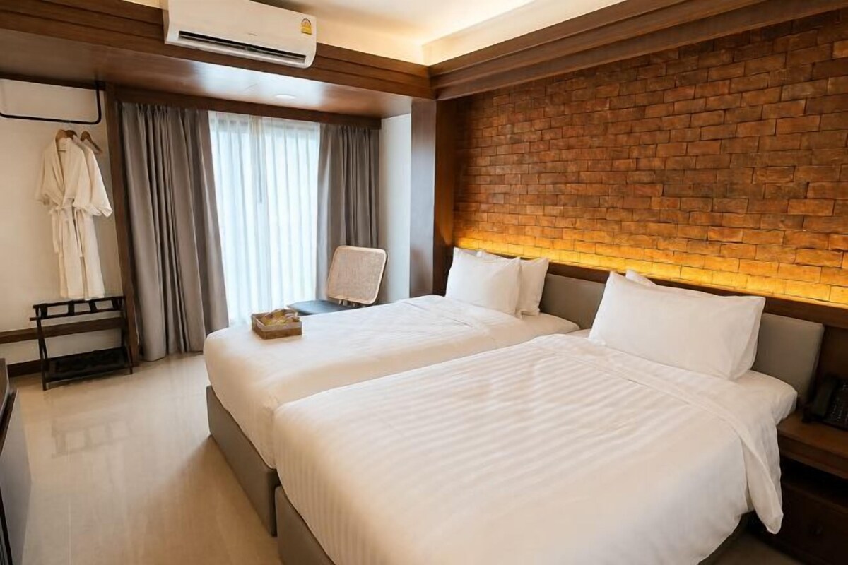 Et hotelværelse med to senge, en mur af mursten som detalje, en bøjle til badekåber og et skrivebord med en stol.