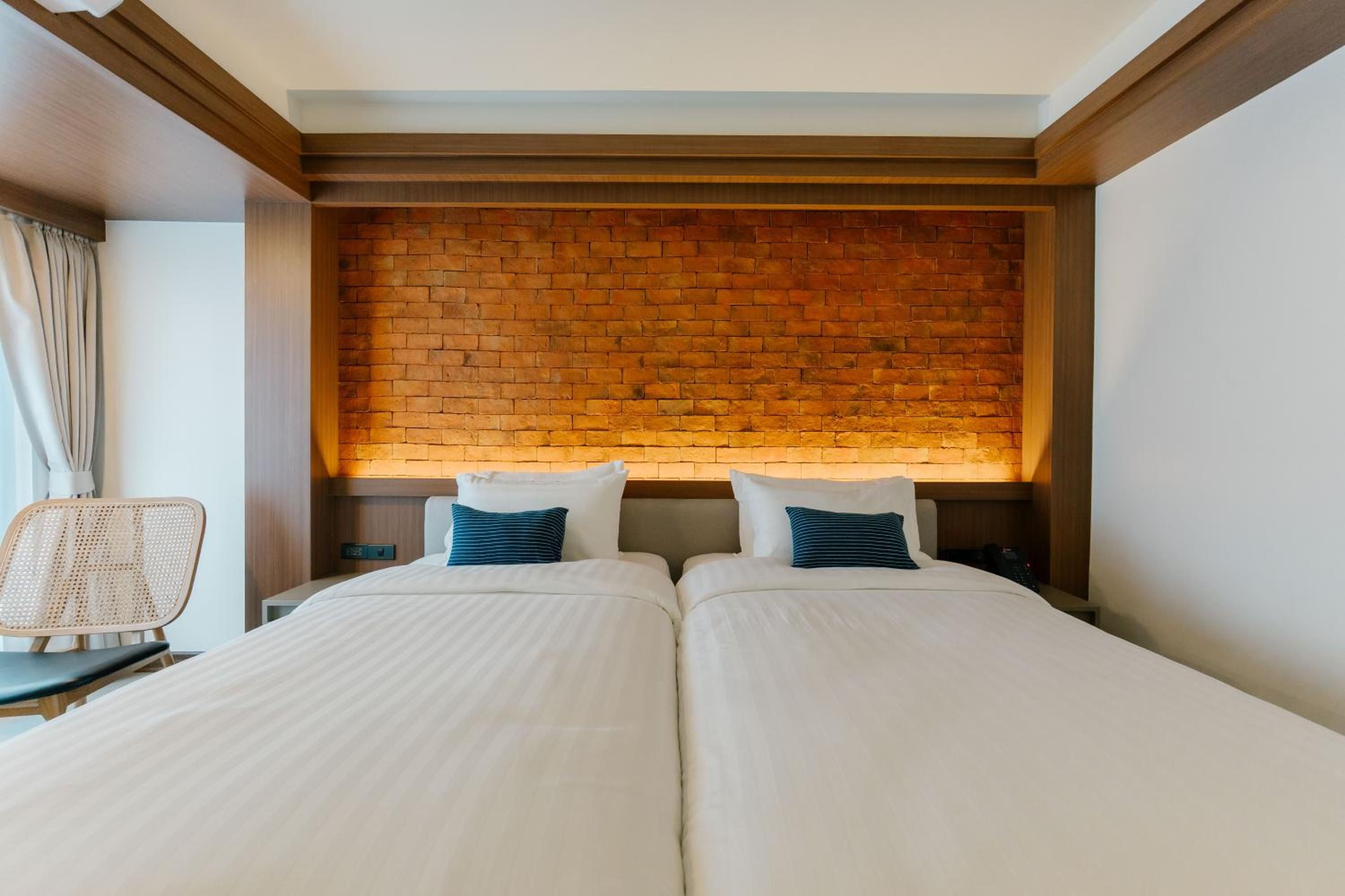 Quarto de hotel com duas camas, parede de tijolos e uma cadeira.