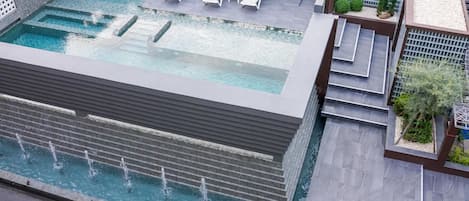 A rooftop pool with multiple levels, water features, and lounge chairs.