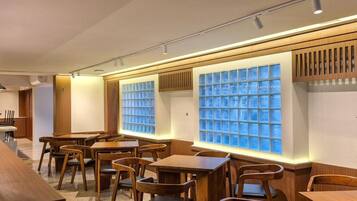 A restaurant interior with wooden tables and chairs, a long counter, and a wall with a grid of blue-tinted windows.