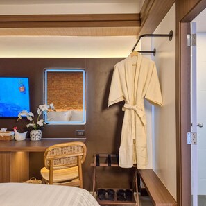 Ein Hotelzimmer mit einem Bett, einem Schreibtisch mit Computer, einem Stuhl, einem an einem Haken hängenden Bademantel und einem Schuhregal.