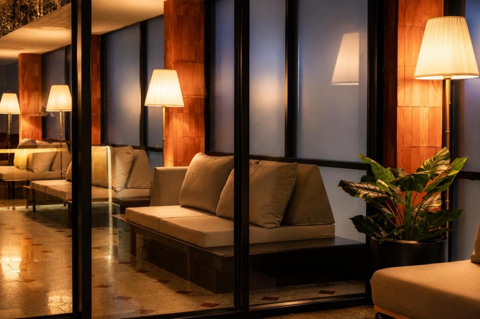 Un vestíbulo de hotel con zonas de estar, lámparas y una gran planta en maceta.