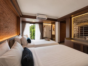A hotel room with two beds, a brick wall, a window with curtains, and a radiator.