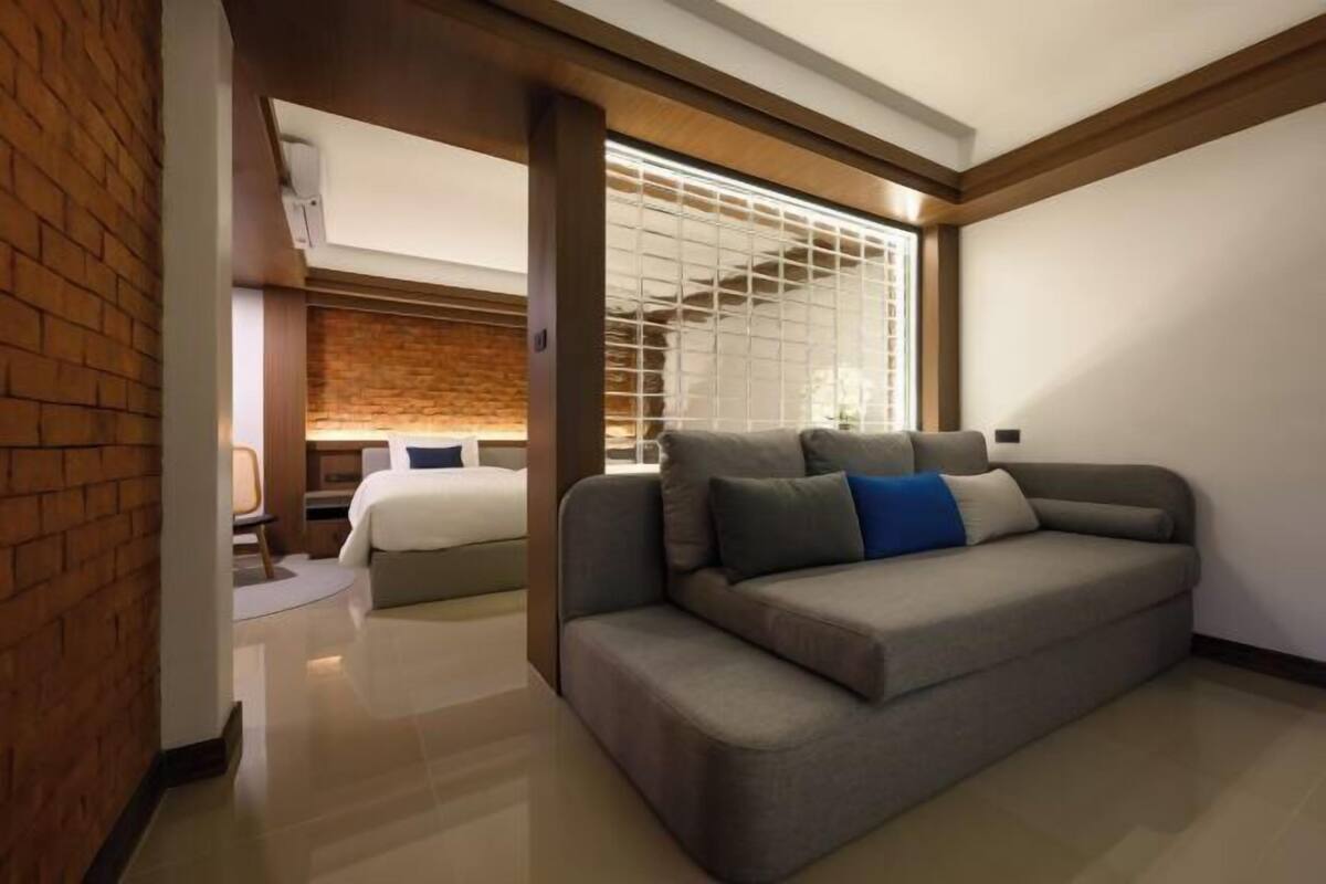 Une chambre d’hôtel moderne avec un canapé gris, un lit et un mur en briques.