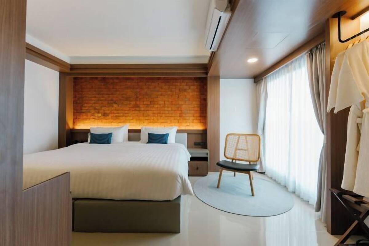 Une chambre d’hôtel moderne avec un mur d’accent en briques, un grand lit, une chaise et une vue sur l’extérieur.