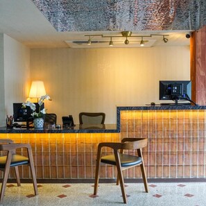 Una zona reception con un banco, sedie, una scrivania, una lampada e un monitor per computer.