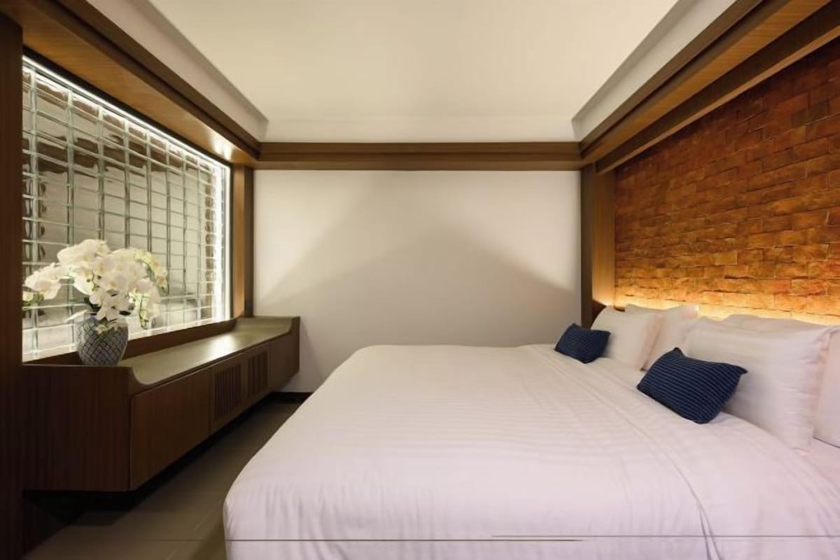 A bedroom with a large bed, a wooden headboard, a window with a view, and a bedside table with a vase of flowers.