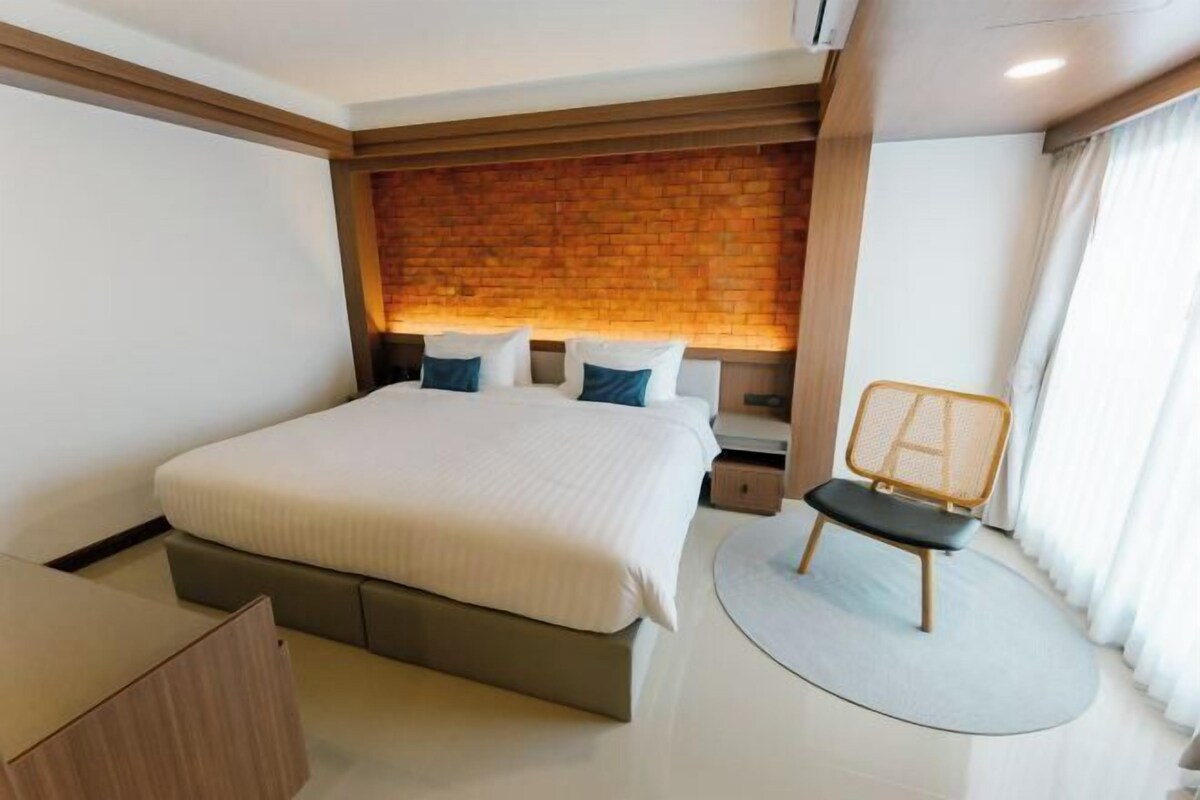Une chambre d’hôtel moderne avec un grand lit, une tête de lit en bois, un petit coin salon et un tapis rond.