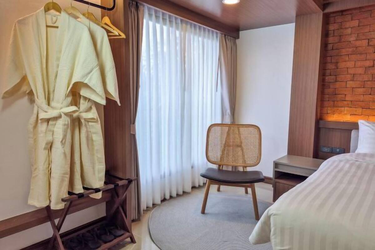 A hotel room with a bed, a chair, a desk, and a hanging robe rack.
