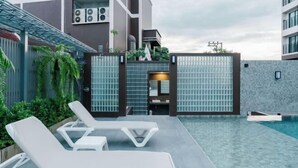 Ein moderner Poolbereich im Freien mit Liegestühlen, einer Glasabtrennung und Blick auf ein Gebäude mit einer Kachelfassade.