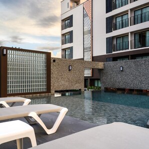 Ein modernes Hotel mit Schwimmbad, Sitzgelegenheiten im Freien und einer Fassade aus Stein und Glas.