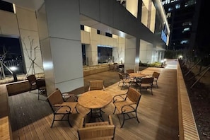 An outdoor seating area with tables and chairs, a wooden deck, and a building in the background. - SUNNY HOUSE (Seoul)