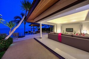A modern living room with a large sofa, a flat-screen TV, and a view of the ocean.