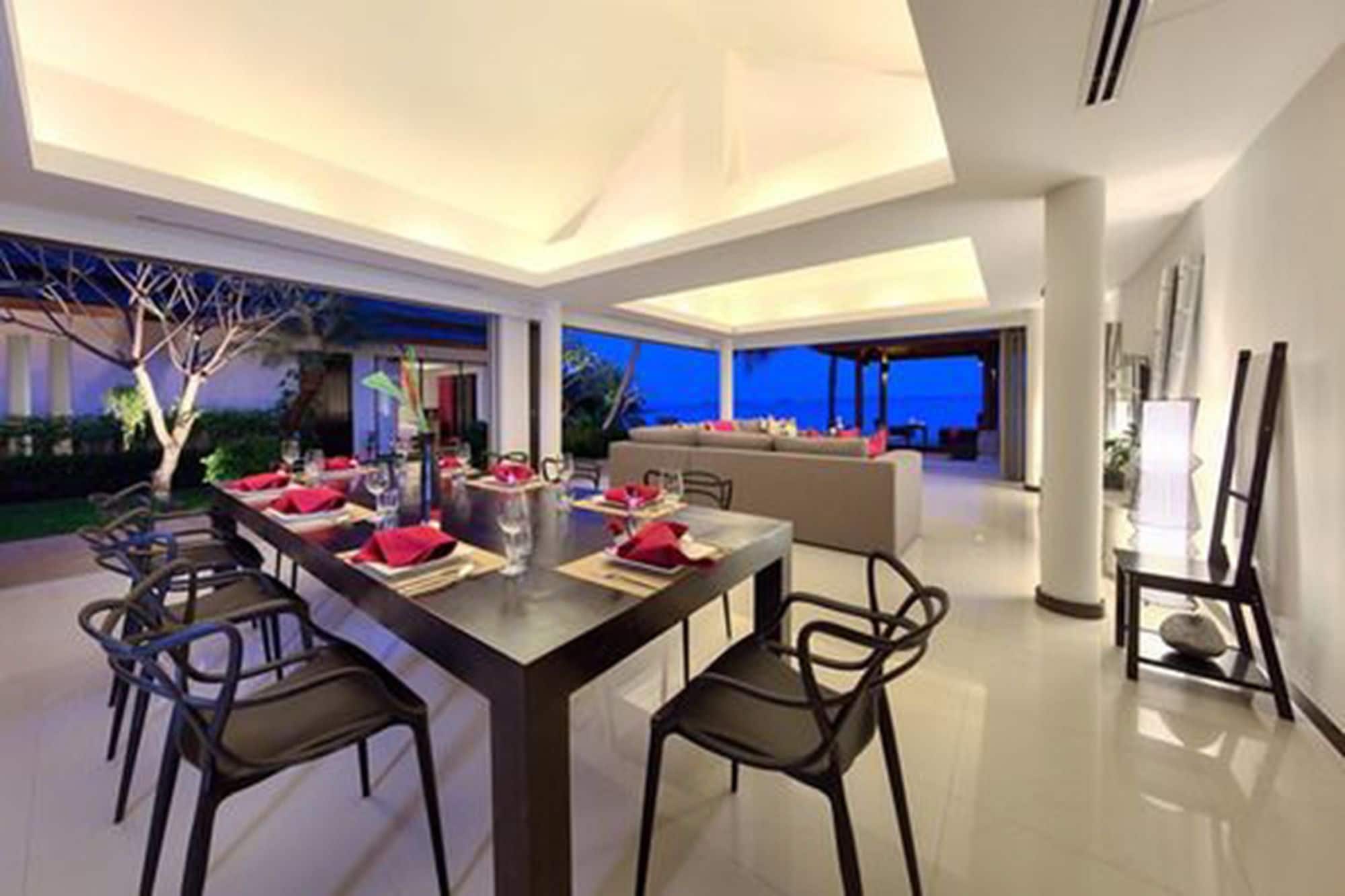 A modern dining area with a long table set for six, surrounded by chairs, and a view of the ocean.