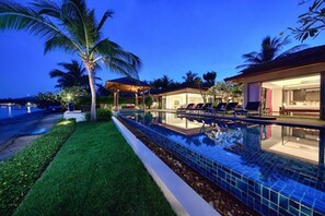 A poolside area with a lounge chair, a palm tree, and a building with a covered patio. - Baan Feung Fah (Koh Samui)