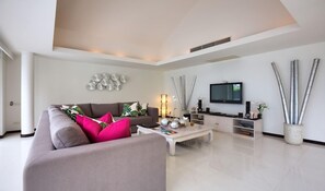 A modern living room with a grey sofa, a coffee table, and a flat-screen TV mounted on the wall. - Baan Feung Fah (Koh Samui)