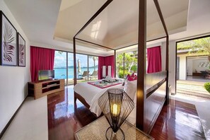 A modern bedroom with a large bed, a bedside table, a lamp, and a view of the sea.