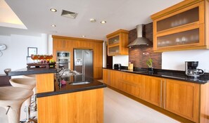 A modern kitchen with wooden cabinets, a stainless steel refrigerator, and a central island with a sink. - Baan Feung Fah (Koh Samui)
