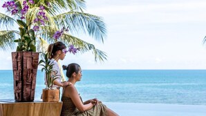 A woman sitting by the ocean with a wooden table and a plant. - Baan Feung Fah (Koh Samui)