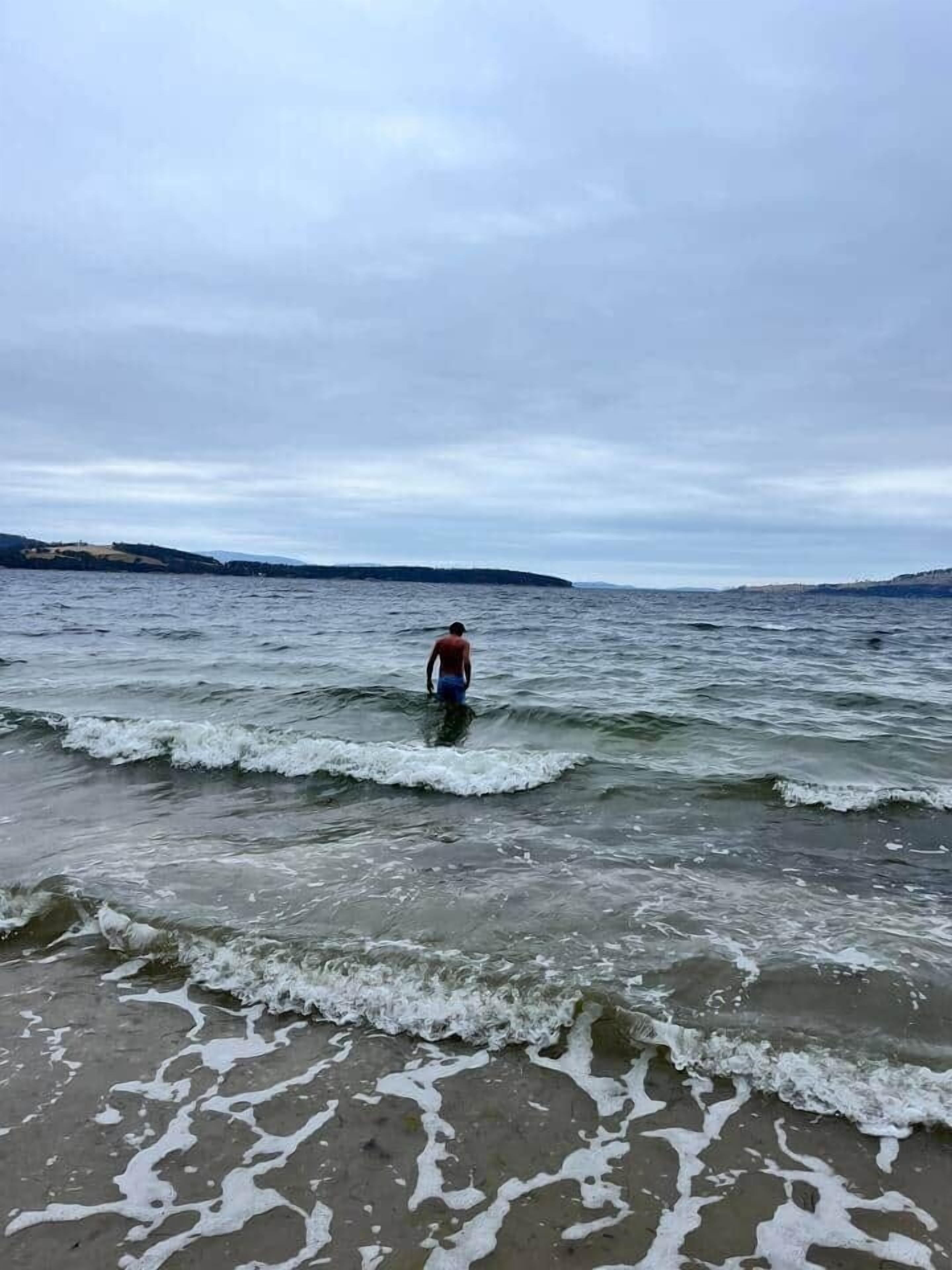 A beach scene with a person walking in the water.
