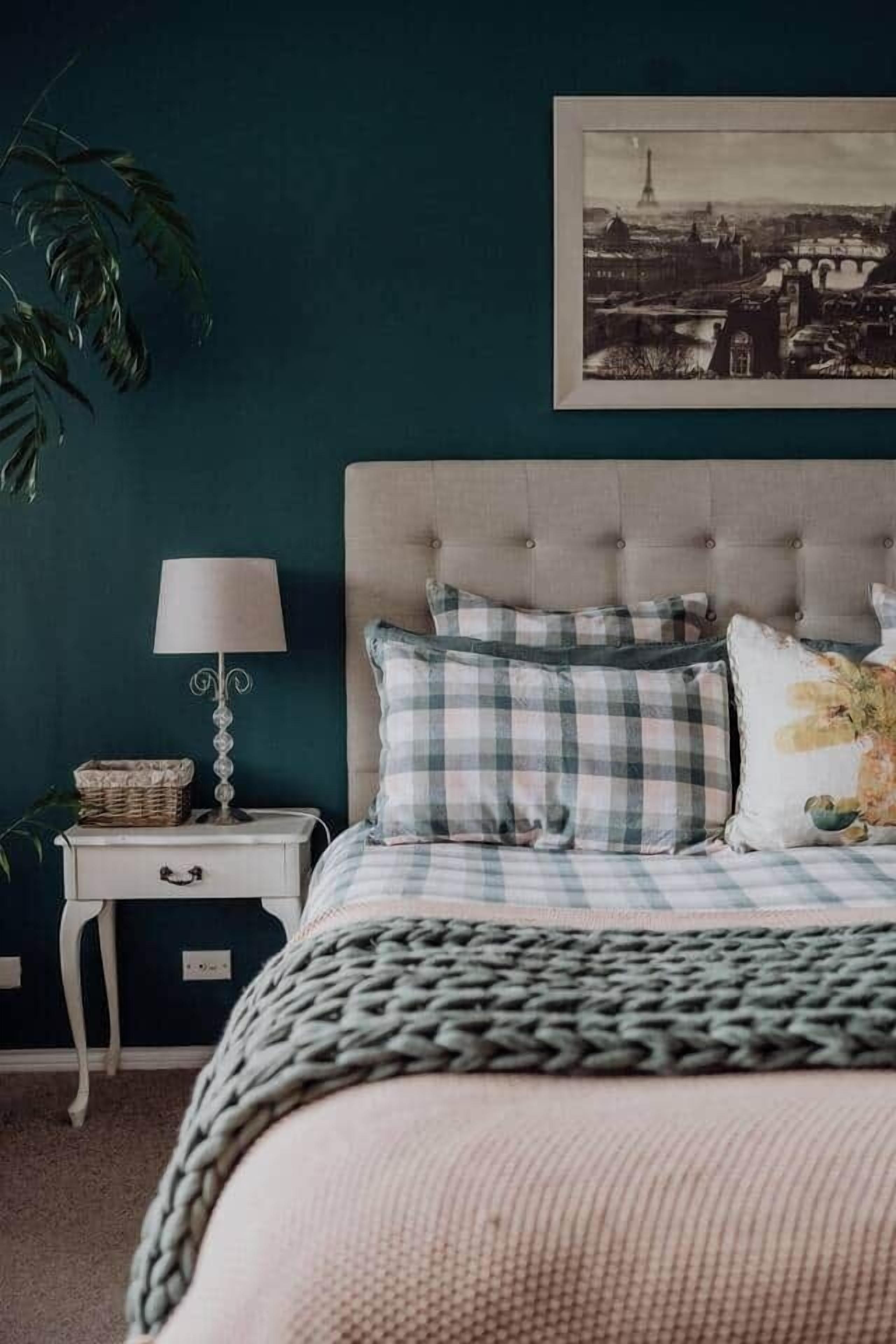 A bedroom with a tufted headboard, a checkered bedspread, and a framed picture of a cityscape.
