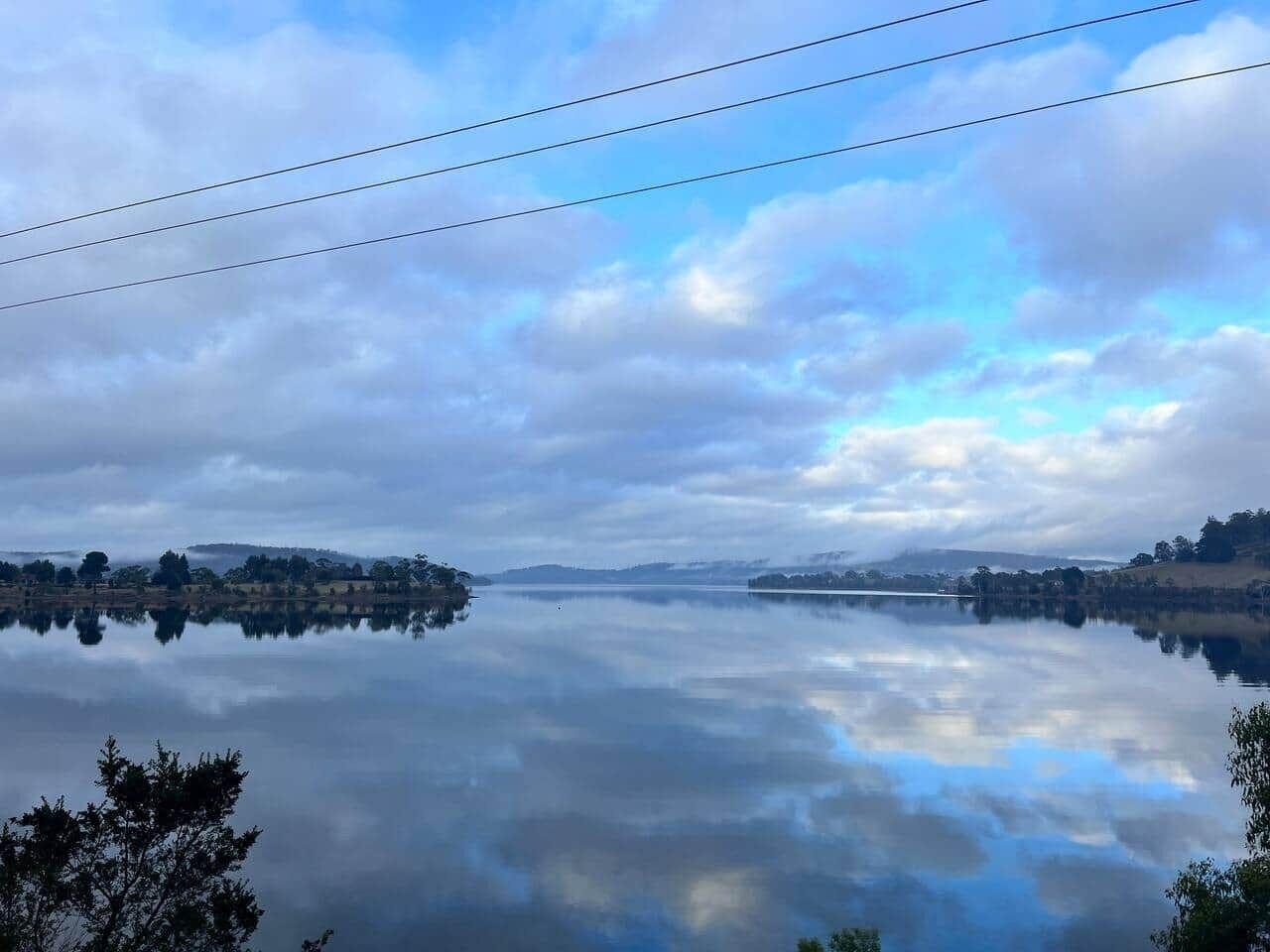A calm lake with a clear reflection of the sky and surrounding landscape.