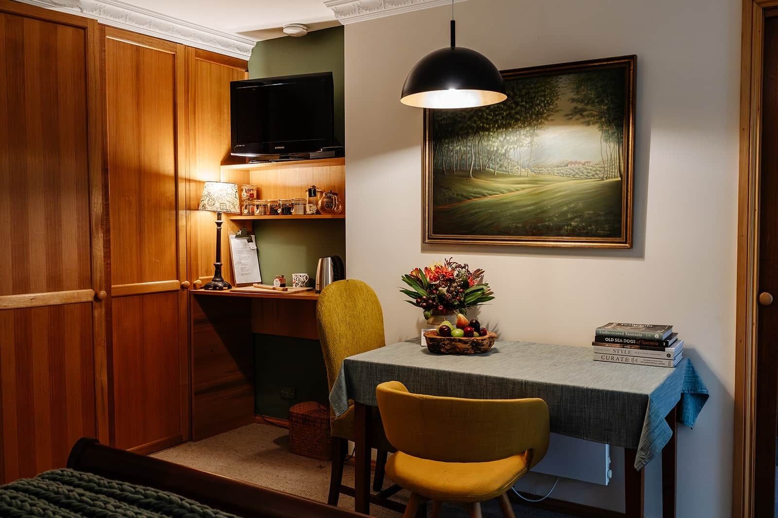 Cocina compacta con armarios de madera, una mesa de comedor con sillas, un cuadro en la pared y un televisor sobre la encimera.