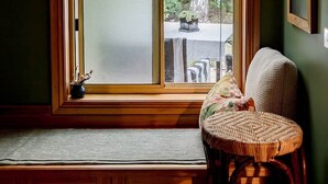 A room with a large window, a wicker chair, and a chandelier. - Peaceful garden setting + Private deck (Gardners Bay)