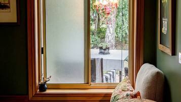 A room with a large window, a wicker chair, and a chandelier.