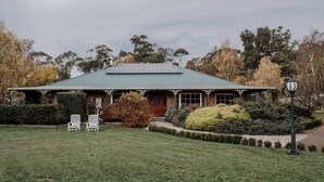 A two-story house with a green roof, a covered porch, and a well-maintained lawn. - Peaceful garden setting + Private deck (Gardners Bay)