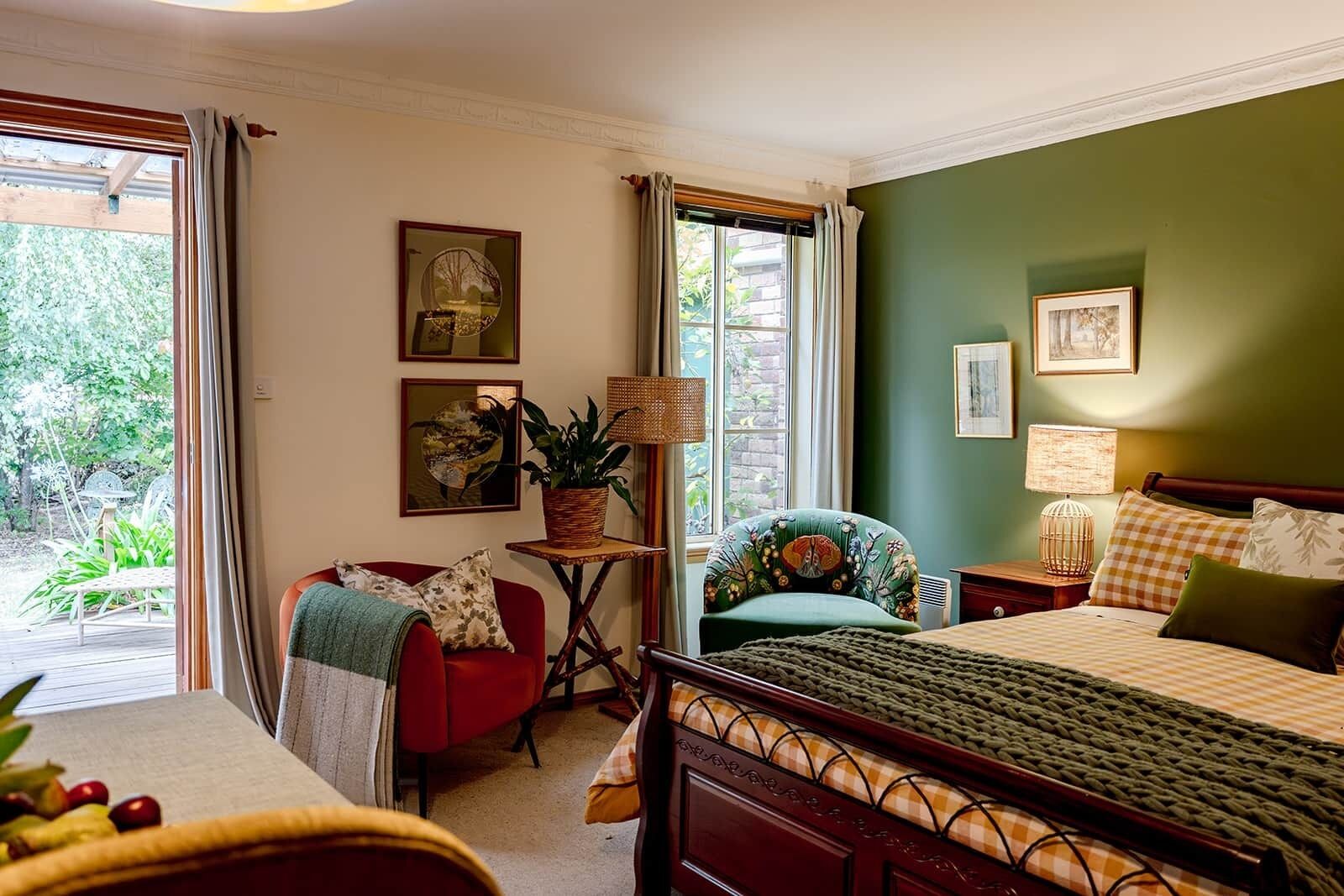 A bedroom with a bed, a chair, a table with a plant, and a window with curtains.
