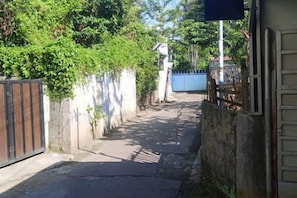 A narrow alleyway with a gated entrance, a blue gate, and a white wall with greenery. - Kos Kosan Mbak Anti (North Bogor)