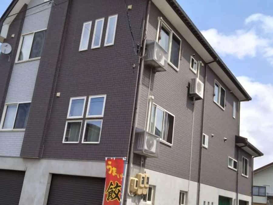 Un edificio de varios pisos con fachada plana, varias ventanas y una unidad de aire acondicionado visible.