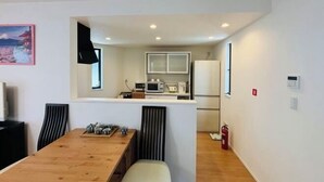 Une cuisine moderne avec des meubles blancs, un four à micro-ondes et un réfrigérateur. On y trouve également un coin repas avec une table et des chaises en bois.
