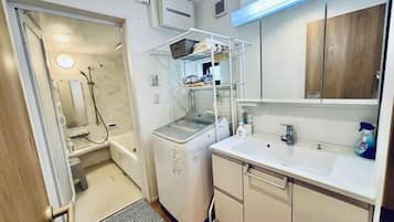 A compact bathroom with a shower, a sink, and a compact washing machine.