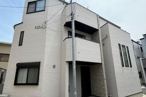 Un bâtiment moderne à deux étages, doté d’un balcon à l’étage supérieur, d’une entrée bien visible et d’une petite fenêtre au rez-de-chaussée.