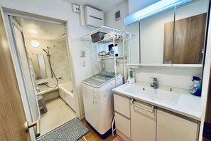 Een kleine badkamer met een douche, een wit wastafeltje en een compact toilet.