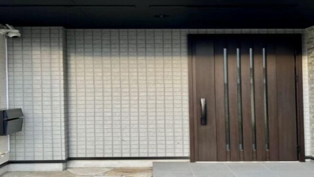 Une entrée moderne, avec un mur recouvert de carreaux, une porte en bois foncé à lattes verticales et un petit espace extérieur agrémenté d’un banc.