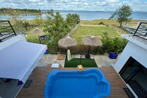 A pool area with a view of the sea, a deck with a table and chairs, and a thatched umbrella. - U-Kham Home View At Sirindhorn (Sirindhorn)